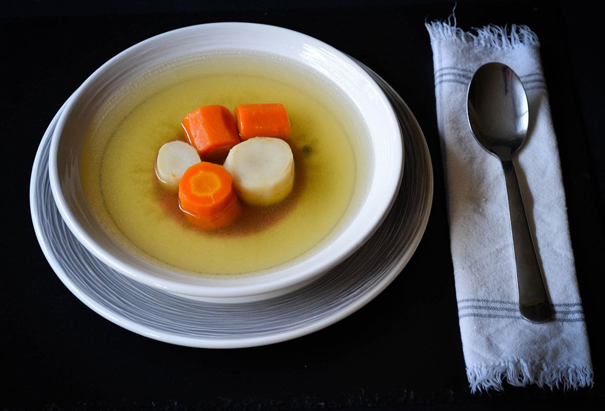 Karácsonyi kacsaleves fehér tányérban zöldségekkel, mellette kanál aszatlkendőn