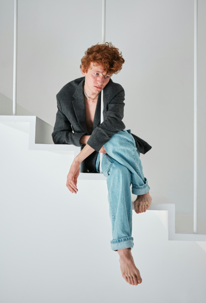 Szomorú fiatal vörös hajú férfi farmerben és zakóban fehér lépcsőn ül