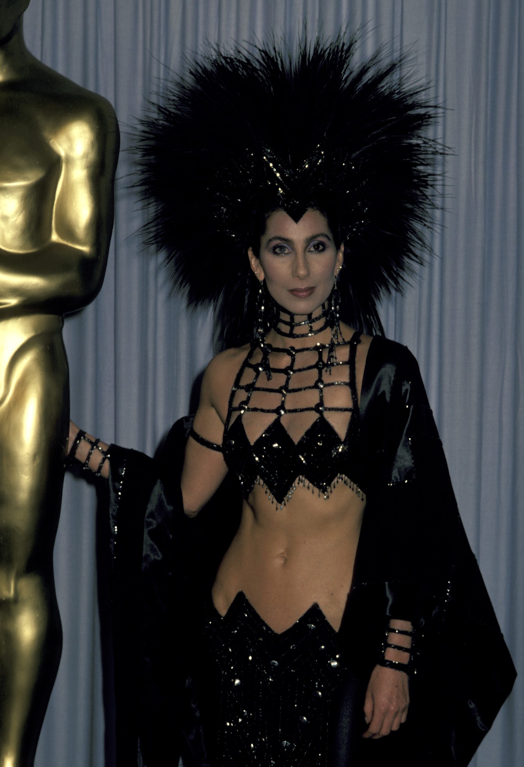 Cher 1986-ban viselte ezt az egyedülálló Bob Mackie fekete flitteres ruhaegyüttest, amely egy felsőből, szoknyából és tollas fejfedőből állt.