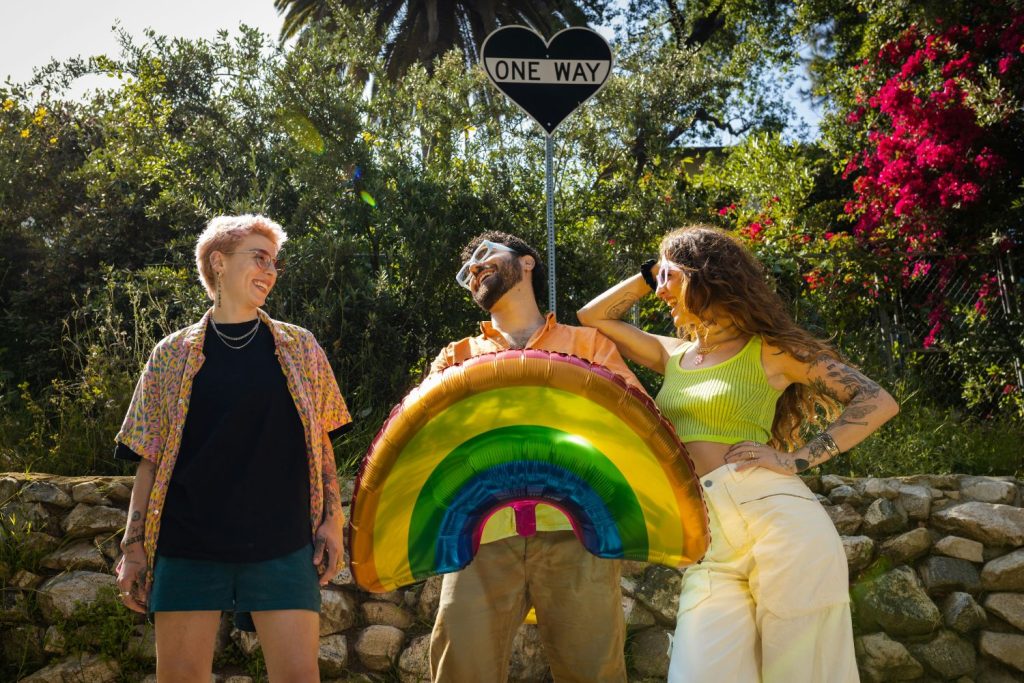 Két nő és egy férfi szivárvány lufit tart a kezében kertben