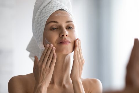 Fiatal nő az arcát krémezi a fürdőszobában