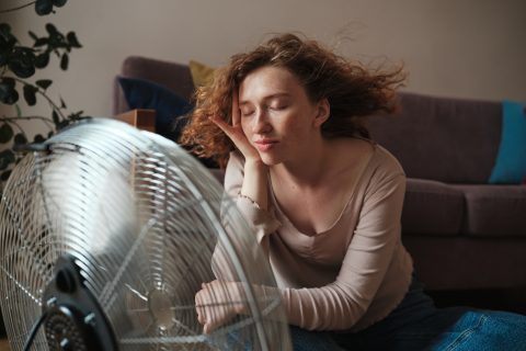 Nő ül a ventillátor előtt csukott szemmel, a haját fújj a levegő