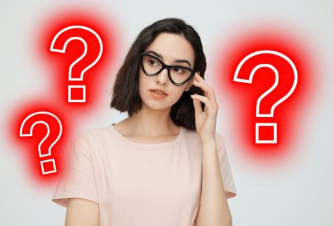 Barna, félhosszú hajú nő fekete vastag keretes szemüvegben, körülötte piros kérdőjelek