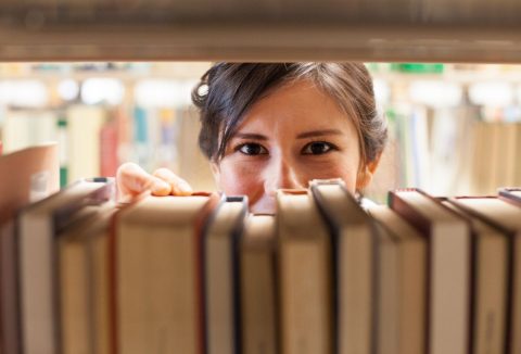 Nő kinéz a könyvek közül a könyvesboltban