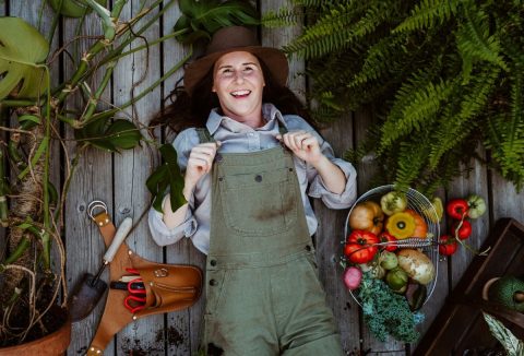 Nő kertésznadrágban növények és kerti szerszámok között