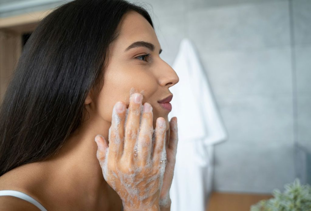 Barna hajú nő habos arclemosóval tisztítja a bőrét