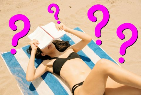 Nő fekete bikiniben könyvvel az arca előtt csíkos strandtörölközőn fekszik a homokban, rózsaszín kérdőjelek