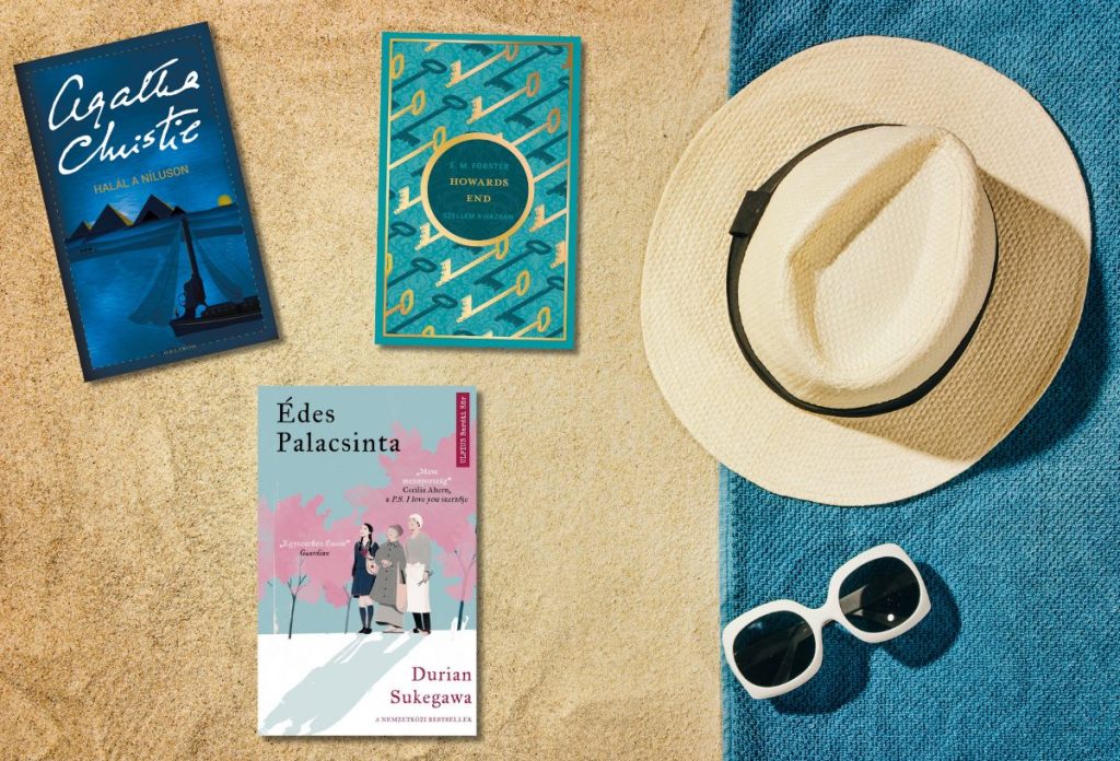 Három könyv borítója a homokban türkiz strandtörölköző, fehér kalap és napszemüveg mellett