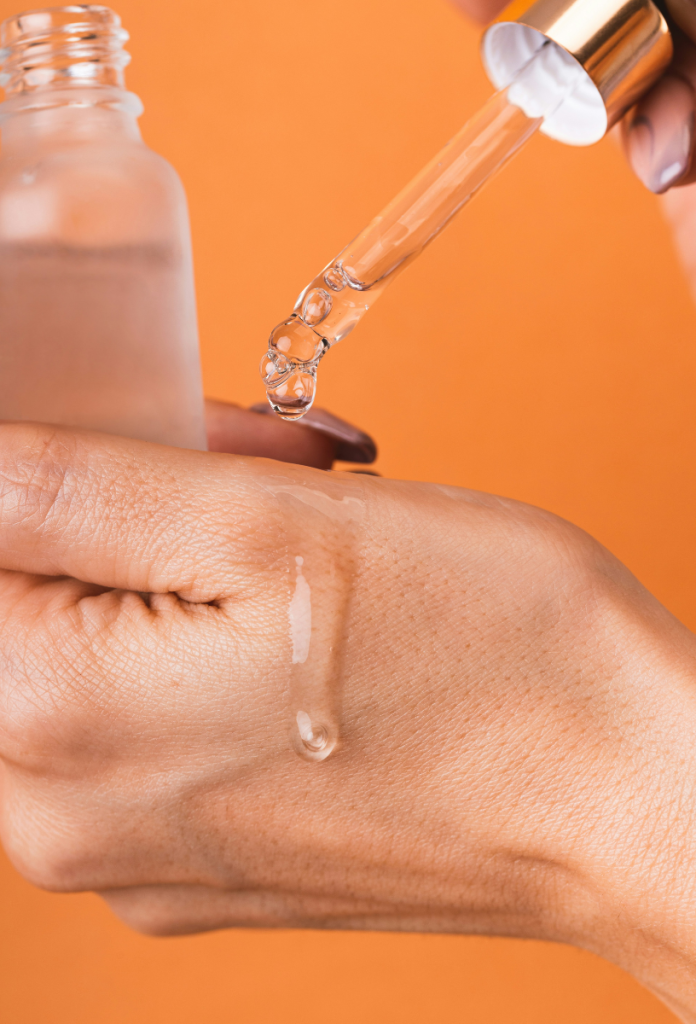 Nő szérumot cseppent a kezére egy üvegcséből a pipettával narancsszínű háttér előtt