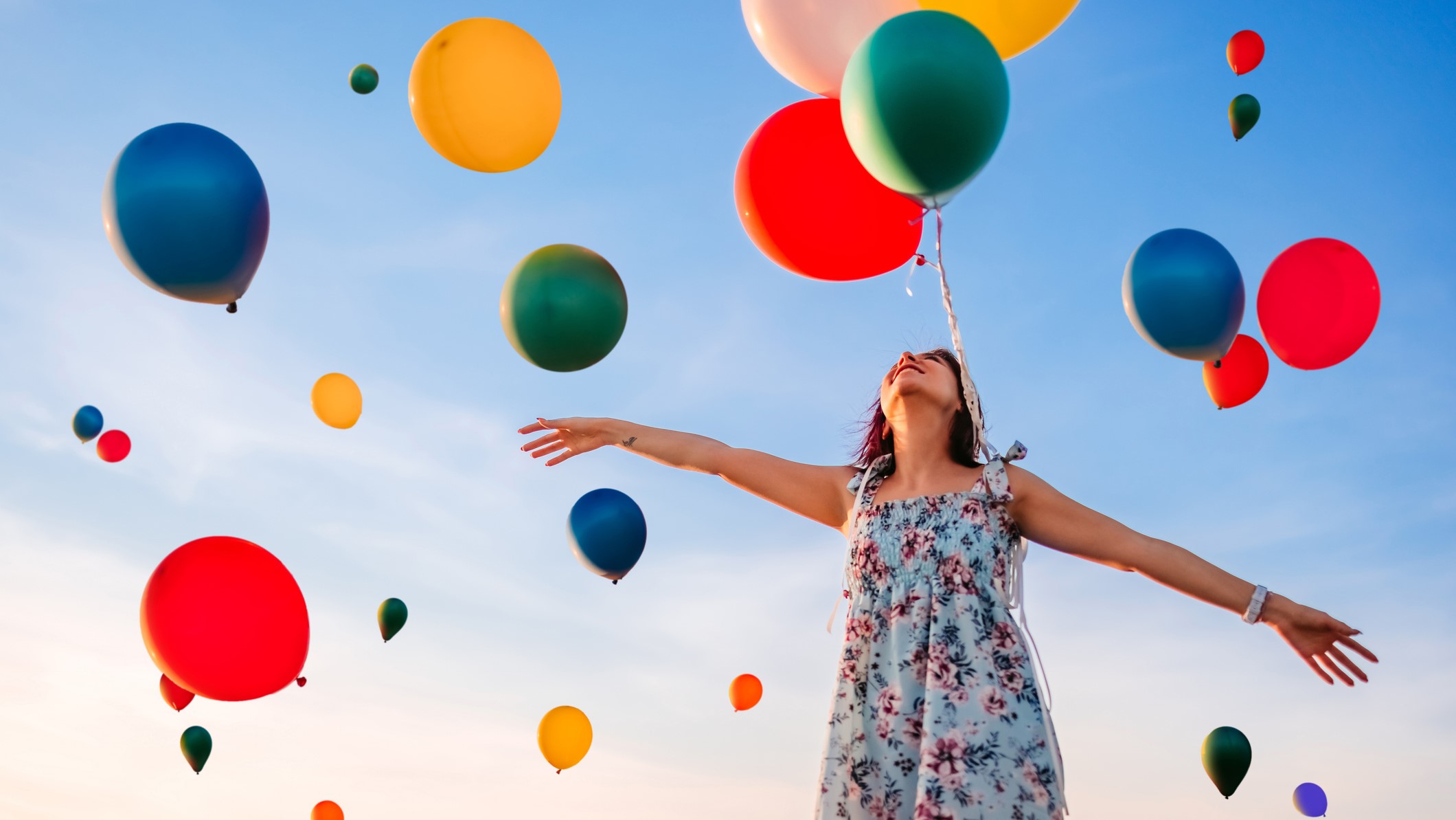 Gyönyörű, mosolygós fiatal nő és léggömbökkel teli égbolt.