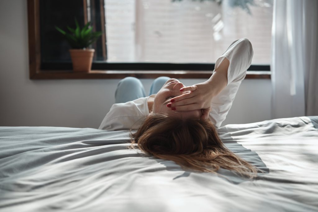 poszttraumas-stressz-ptsd-tunetek-es-kezelese | Marie Claire Fiatal nő magányosan, kimerülten ül a földön, fejét az ágyon hátraveti és eltakarja arcát