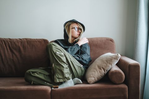 Magányos, depressziós nő ül a kanapén, kifelé néz, magát öleli