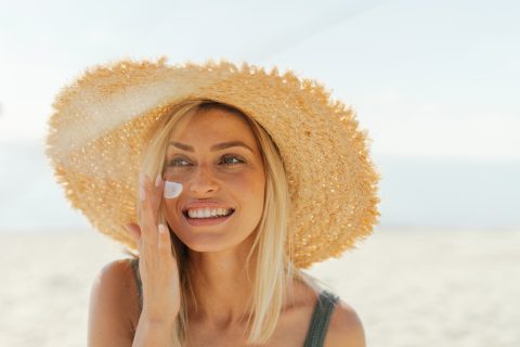 Fiatal nő fényvédőt ken az arcára a strandon