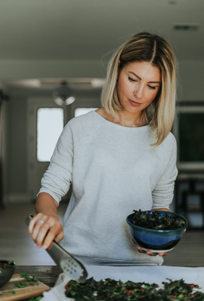 Szőke nő fehér felsőben leveles zöldségeket tesz tálba