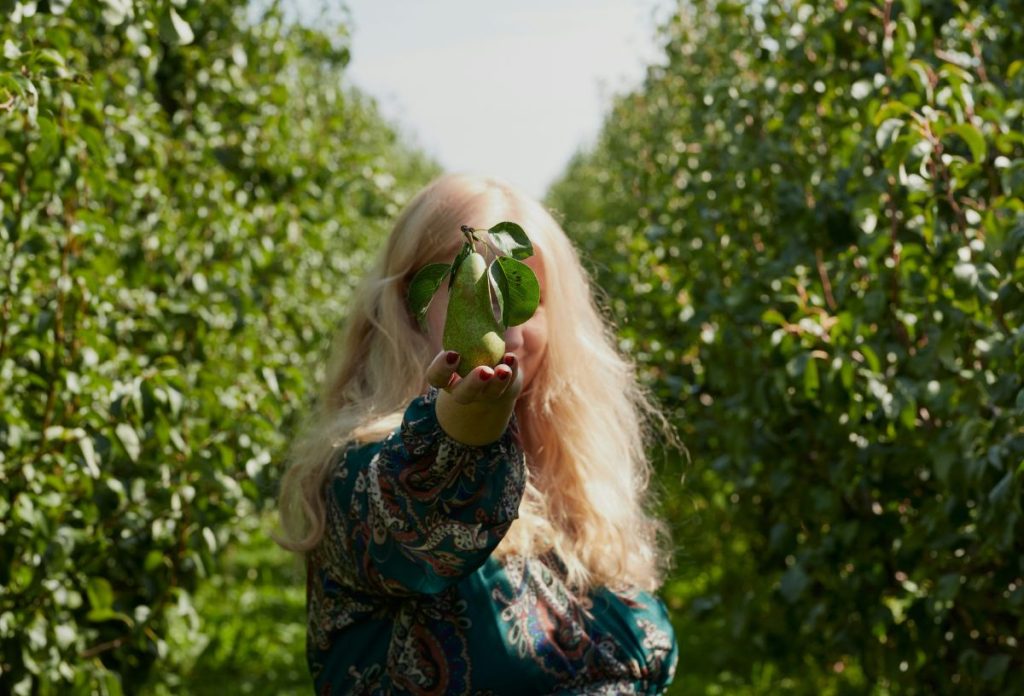 Szőke, hosszú hajú nő érett körtét tart az arca elé ősszel