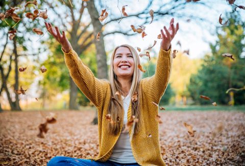 Egészséges fiatal szőke hajú nő őszi faleveleket dob a feje fölé