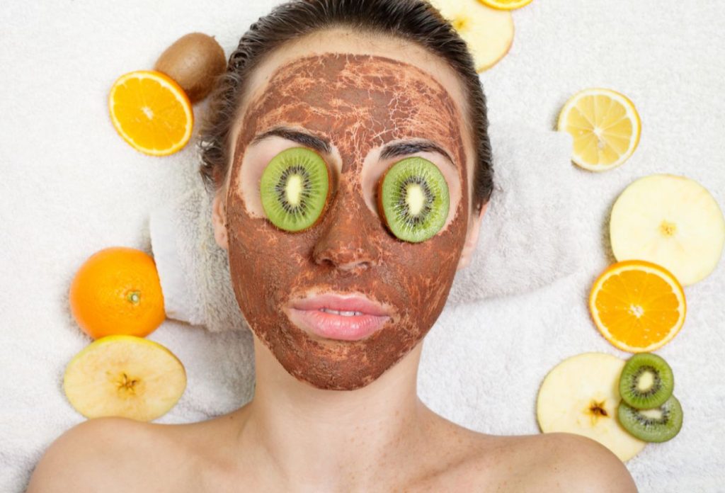 Nő házilag készített arcpakolással, körülötte gyümölcsszeletek