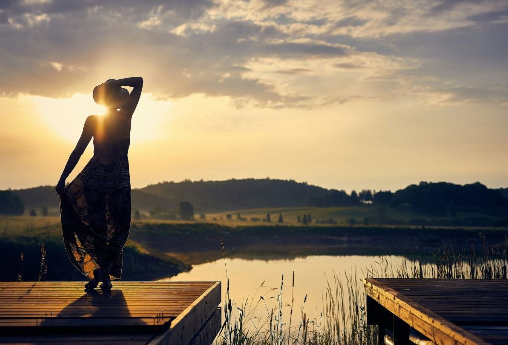 Nő hosszú ruhában a stégen áll nyári naplementében