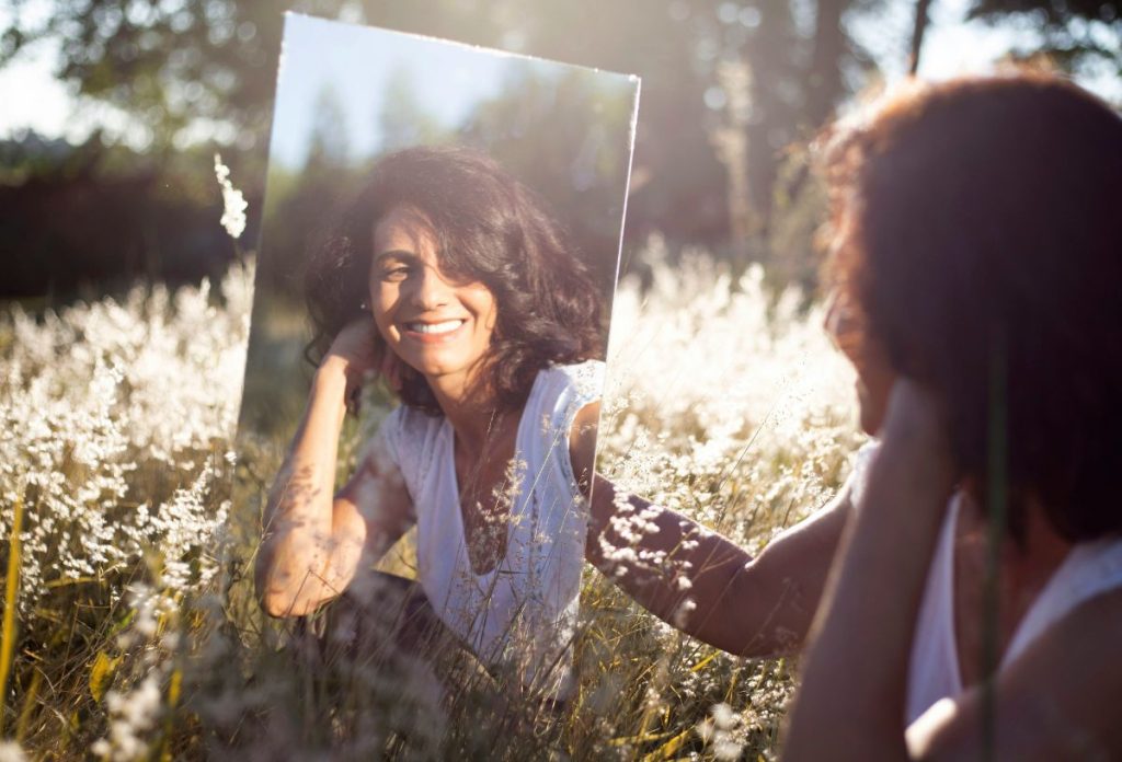 Nő egy mezőn ülve tükörben nézi magát