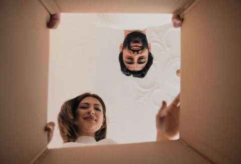 Barna hajú nő és fekete hajú, szakállas férfi hajol egy kartondoboz fölé, alulnézetből látjuk