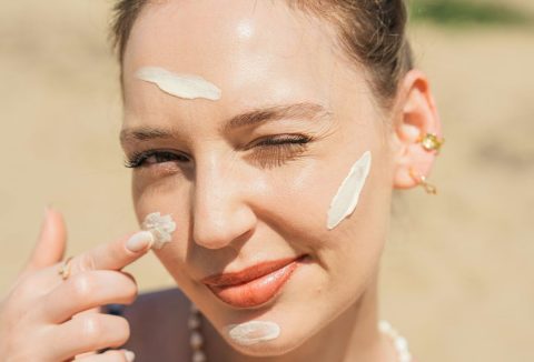Szép, fiatal nő fényvédő krémet ken az arcára