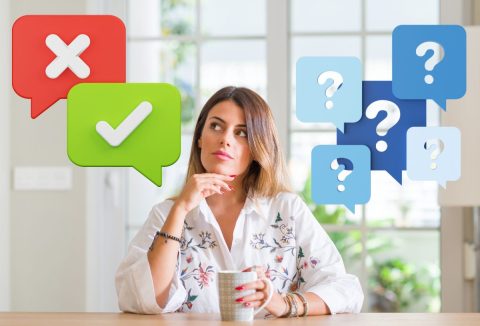 Hosszú hajú nő kávéspohárral a kezében gondolkodik a helyes válaszon, kérdőjelek és jó válasz-rossz válasz jel mellette