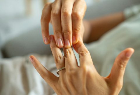 Nő egyik kezével a másikat simítja, az ujján gyűrű van