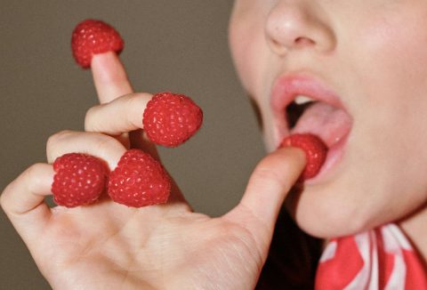 Nő az ujjai végén málnával a hüvelykujját a szájába veszi