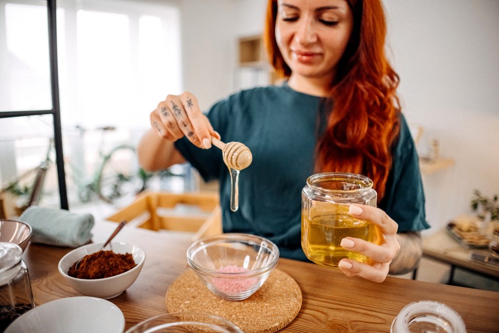  Vörös hajú nő mézet csorgat egy tálba arcpakolás készítéséhez