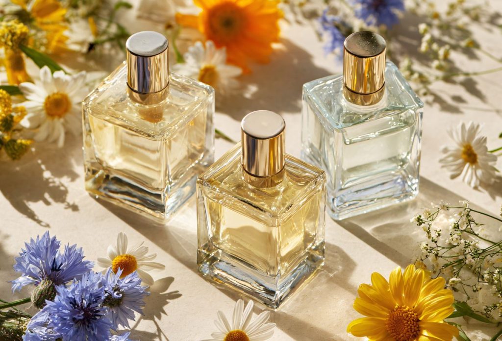 Nyári virágok között sárgás árnyalatú parfümös üvegek