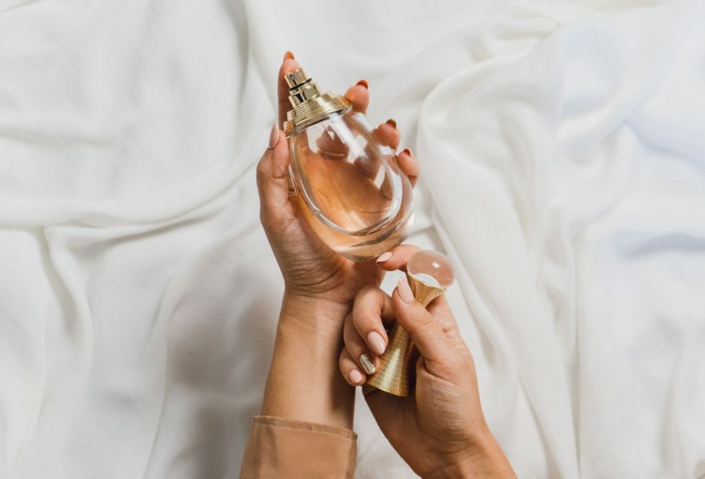 Fehér selyem háttér előtt nő csepp alakú parfümös üveget fog