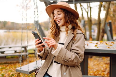 Egy kabátot és kalapot viselő nő telefonozik az őszi időben