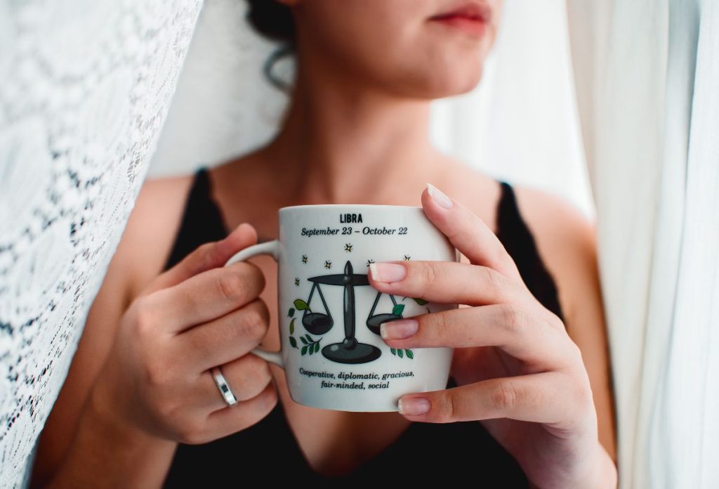 nő mérleg csillagjeggyel díszített fehér bögrét tart a kezében