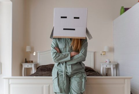 nő pizsamában, egykedvű arcú kartondobozzal a fején