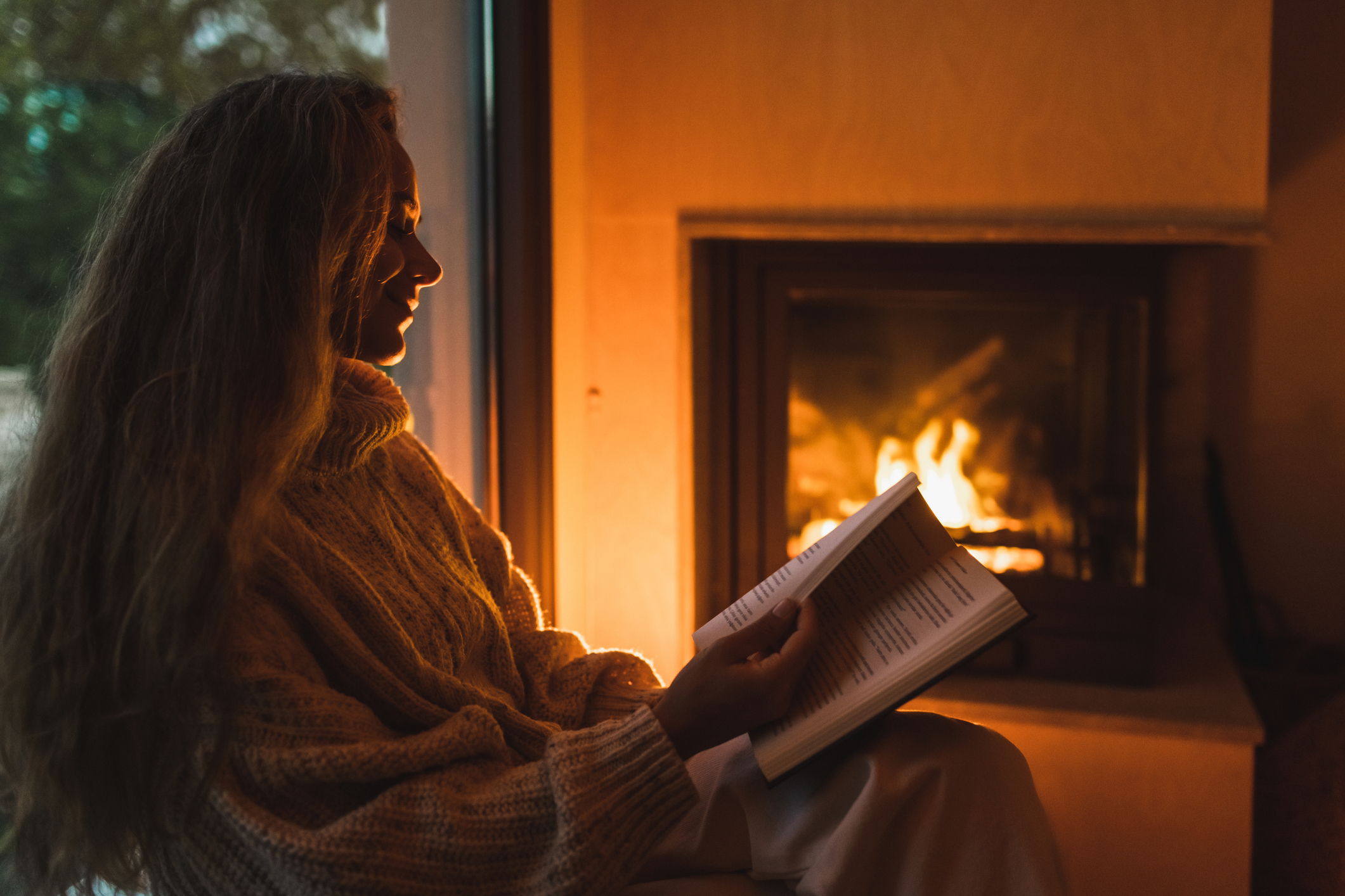 Fiatal nő este a kandalló mellett olvas.
