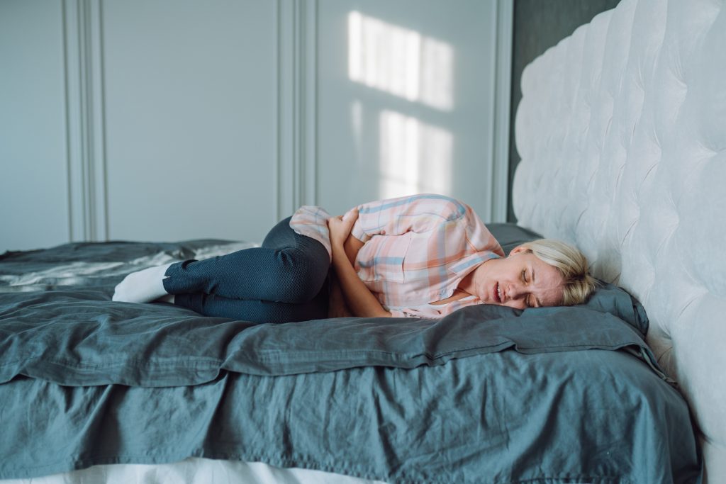 Fájdalomtól összegörnyedő fiatal nő fekszik az ágyon