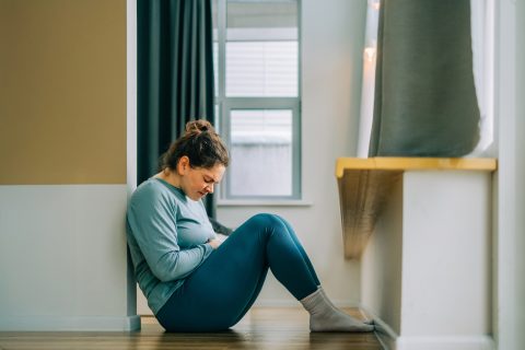 Fájdalomtól összegörnyedő fiatal nő földön ül