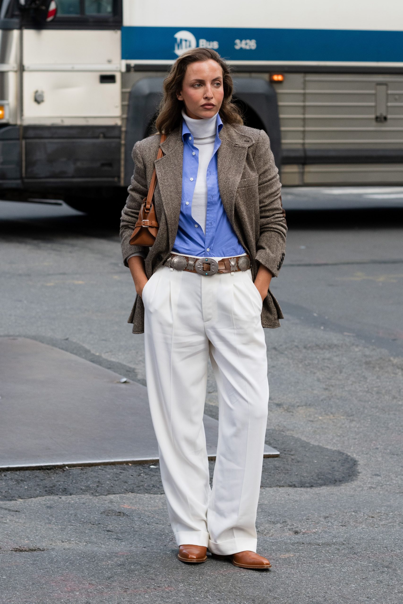 Egy nő barna blézerben, kék ingben, fehér garbó felsőben és fehér nadrágban láttak, barna csizmával és barna táskával.