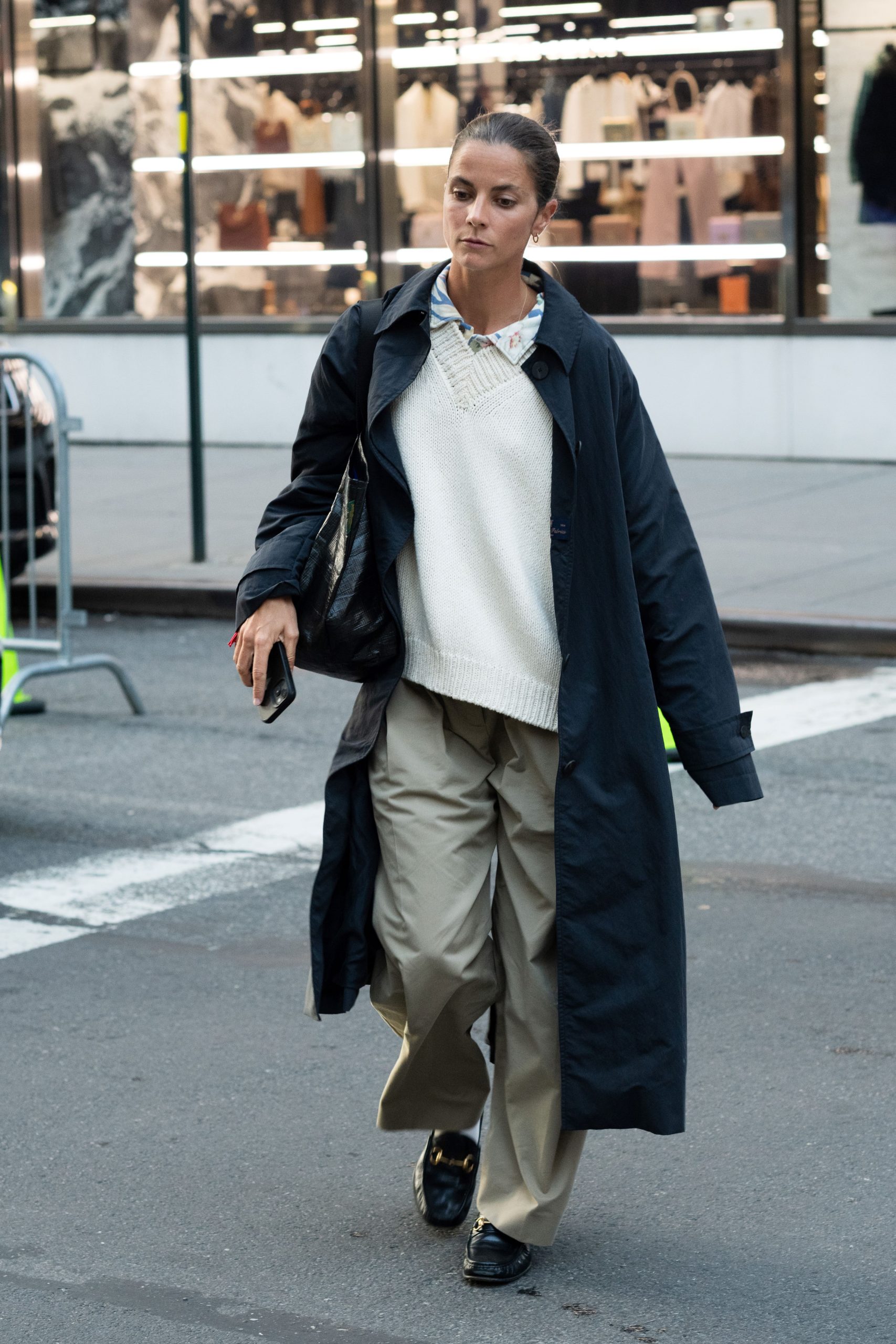 Egy nő tengerészkék trench kabátban, fehér pulóverben, khaki nadrágban és fekete loafer cipőben láttak.