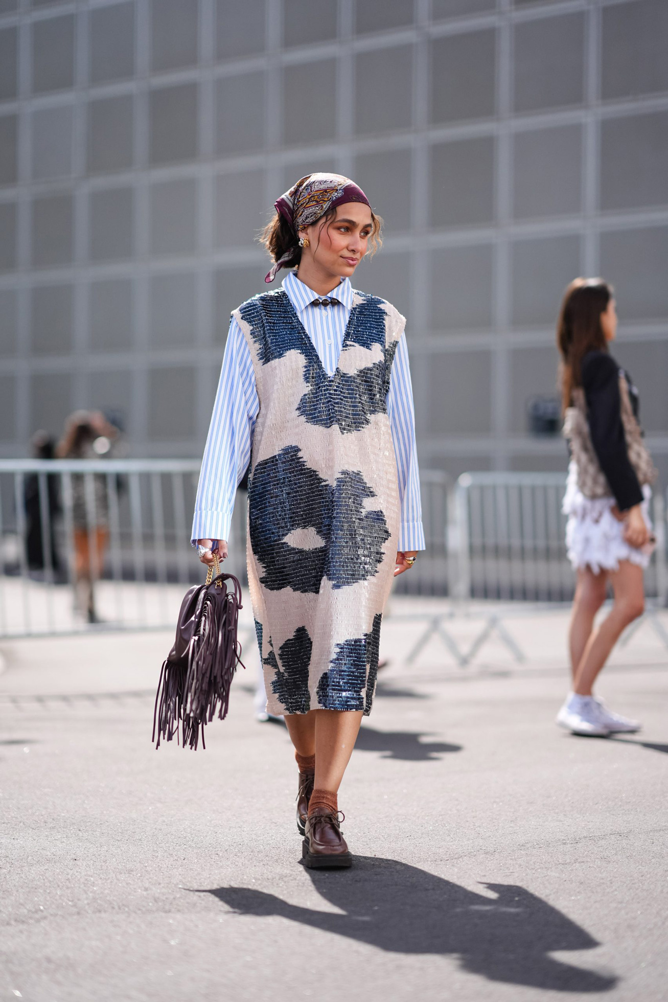 Egy fejkendőt viselő nő kék ingben és hosszú tarka ruhában