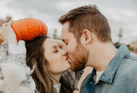 Csókolózó pár, a nő egy narancssárga sütőtököt tart a feje fölé