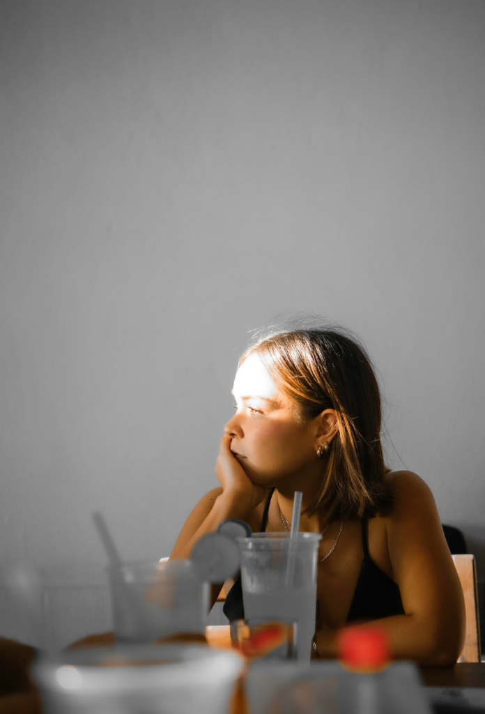 Unatkozva távolba néző nő könyököl asztalon, előtte poharak