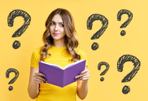 Sárga pólós, hosszú barna hajú fiatal nő lila könyvből olvas, sárga háttér, fekete kérdőjelek