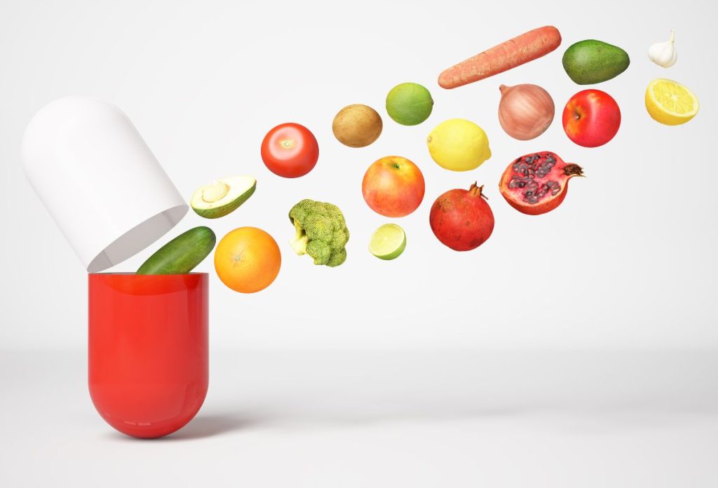 fehér-piros kapszulába zöldségek, gyümölcsök repülnek bele, koncepciófotó multivitamin szedéshez