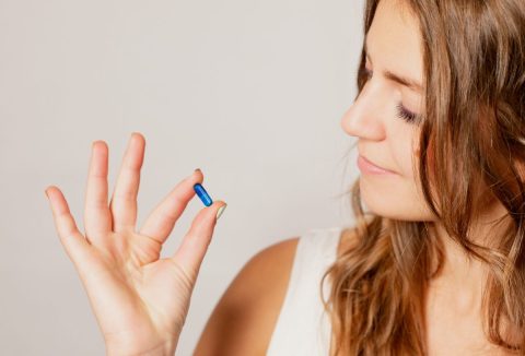 Barna hajú nő a kezében tartott kék színű kreatin kapszulát nézi