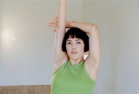 Barna, félhosszú hajú nő zöld felsőben felemelt karokkal