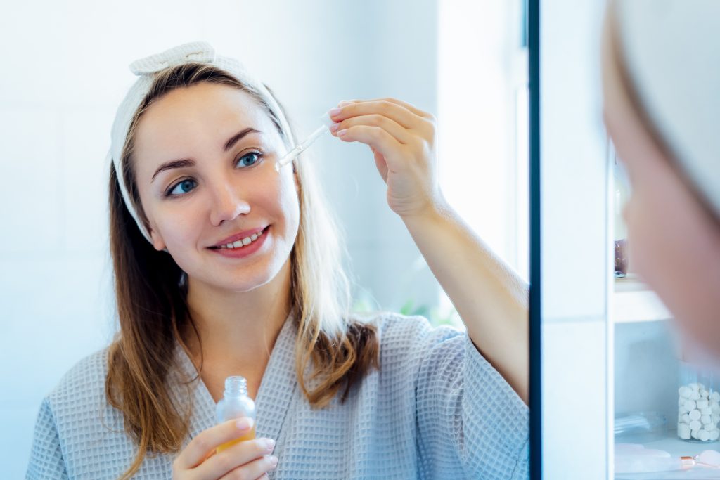 fiatal nő szérummal keni be magát a tükör előtt