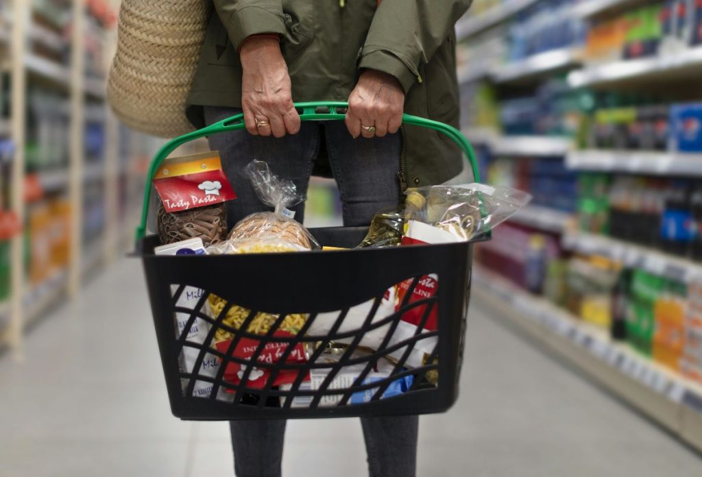 Nő teli bevásárlókosárral áll a szupermarketben