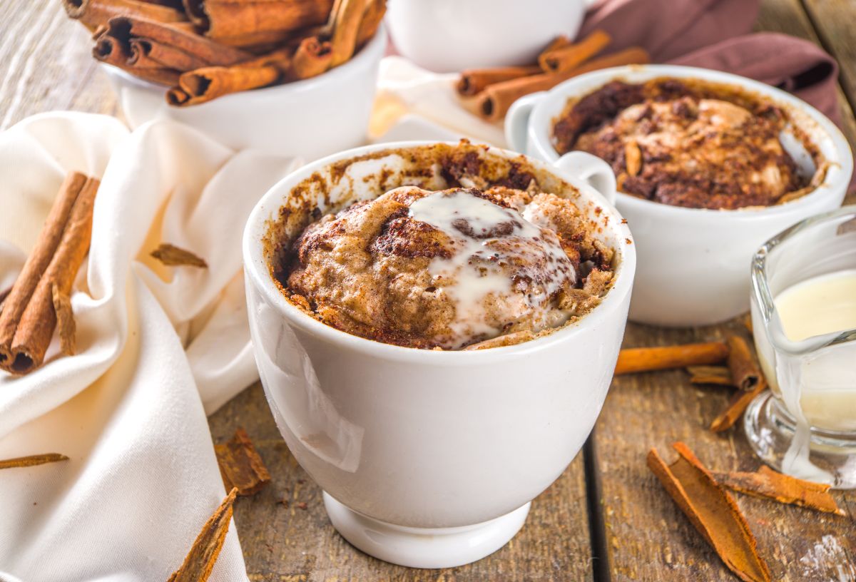 Fahéjas bögrés kuglóf fehér csészében, körülötte különböző hozzávalók, fahéj