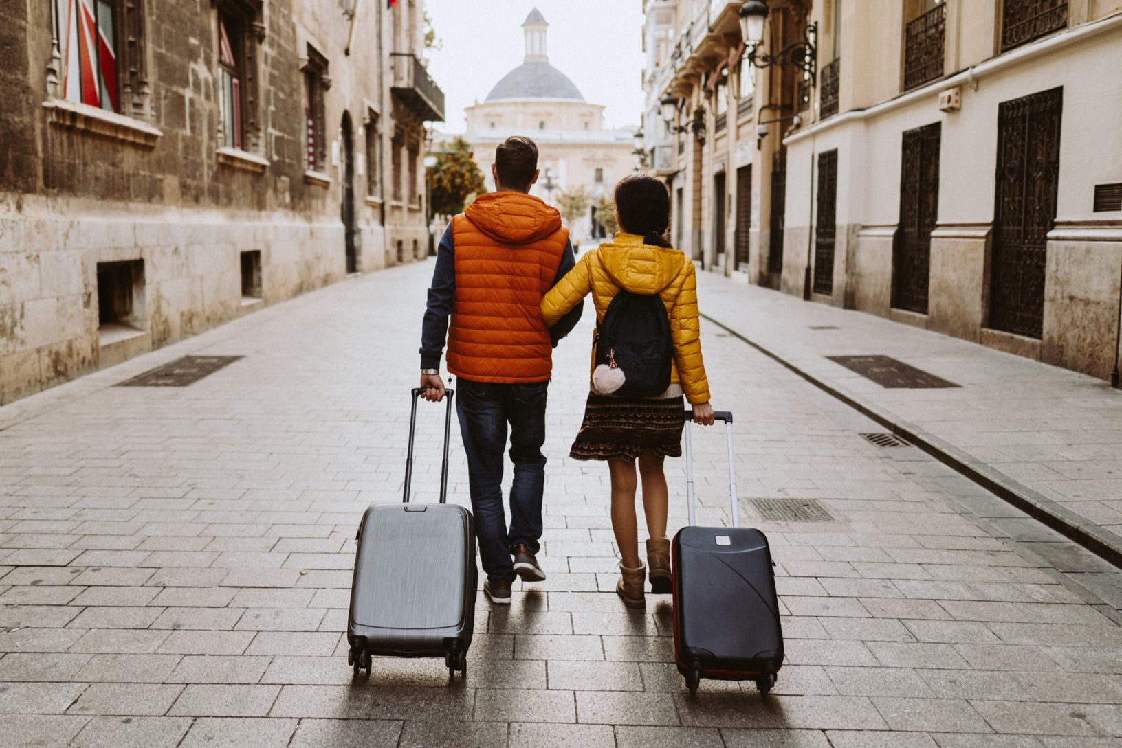 Pár kézenfogva sétál utazóbörődökkel